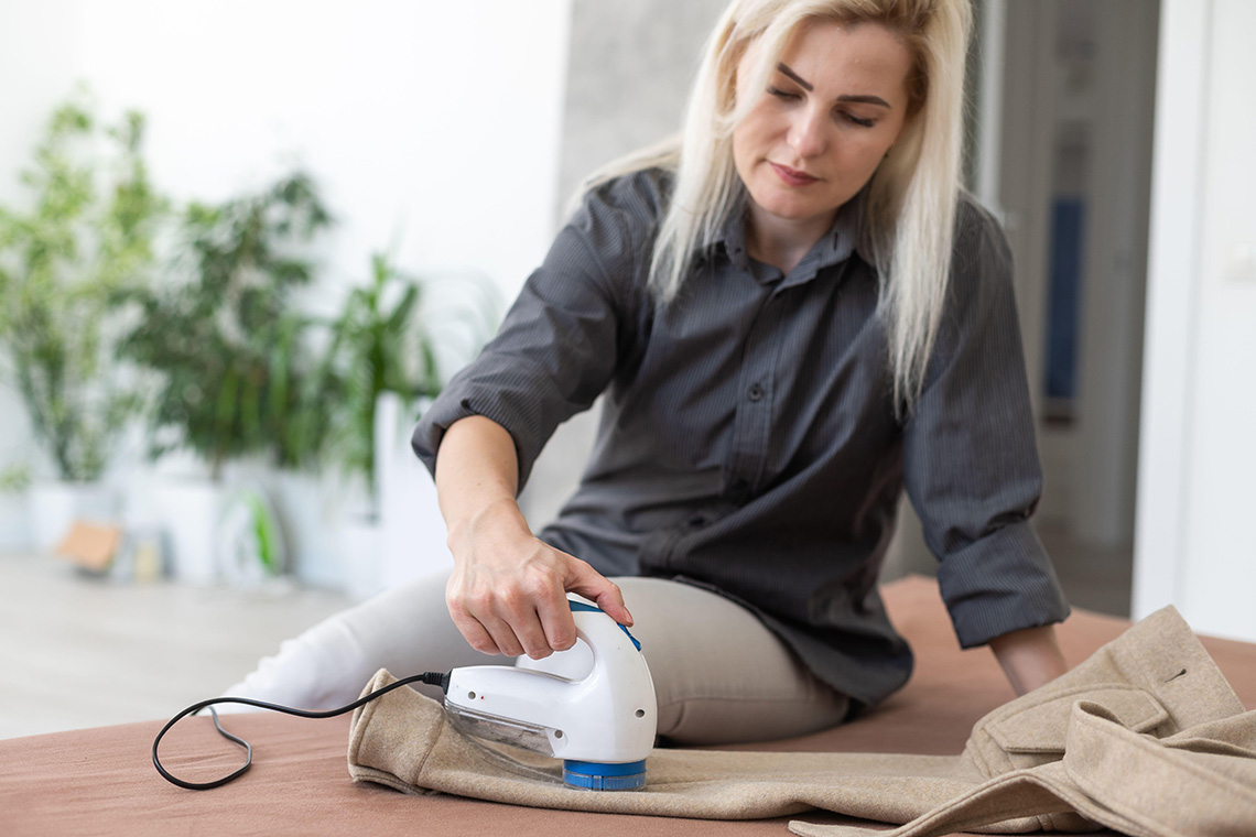 A woman uses a fabric shaver for removing pellet and spools from clothes and fabric on trousers