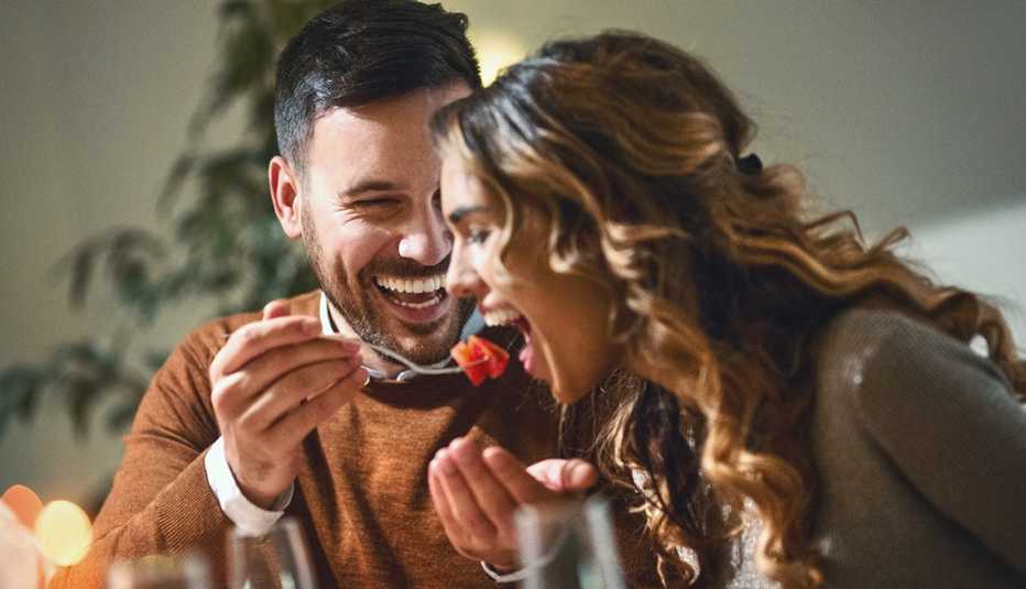 Closeup of mid 20's couple having fun during dinner party. The guy is feeding his girls with some chopped fruit, both laughing.