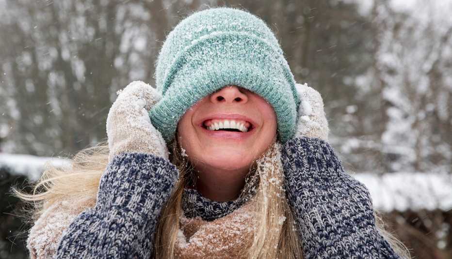 a woman in snowy weather pulling down her knit hat and smiling a woman in snowy weather pulling down her knit hat and smiling