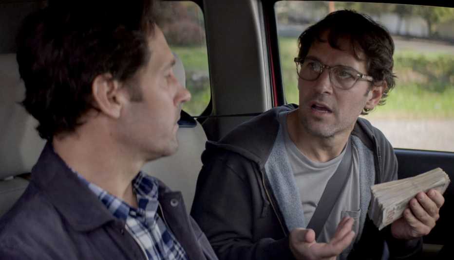 A scene inside a car, Paul Rudd holds money while talking to Paul Rudd in the limited Netflix series 'Living with Yourself'