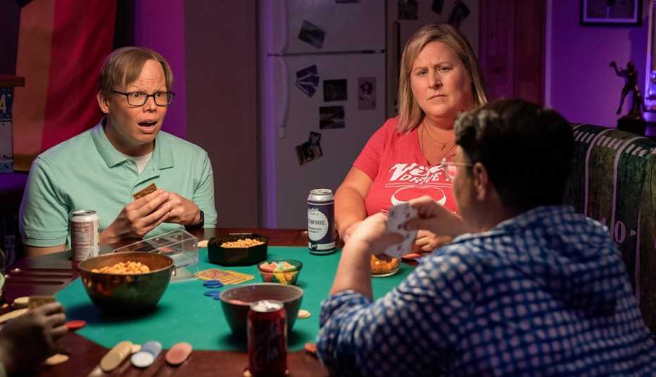 three people sitting at table playing cards with snacks and drinks on the table in still from somebody somewhere