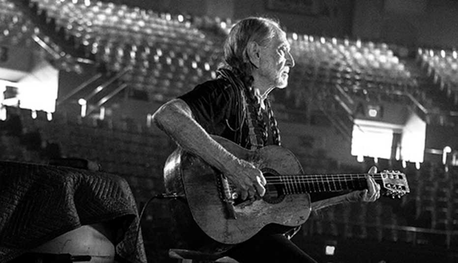 Wille Nelson sitting on a stool playing a guitar on stage. Box reads "Willie Nelson & Family" 