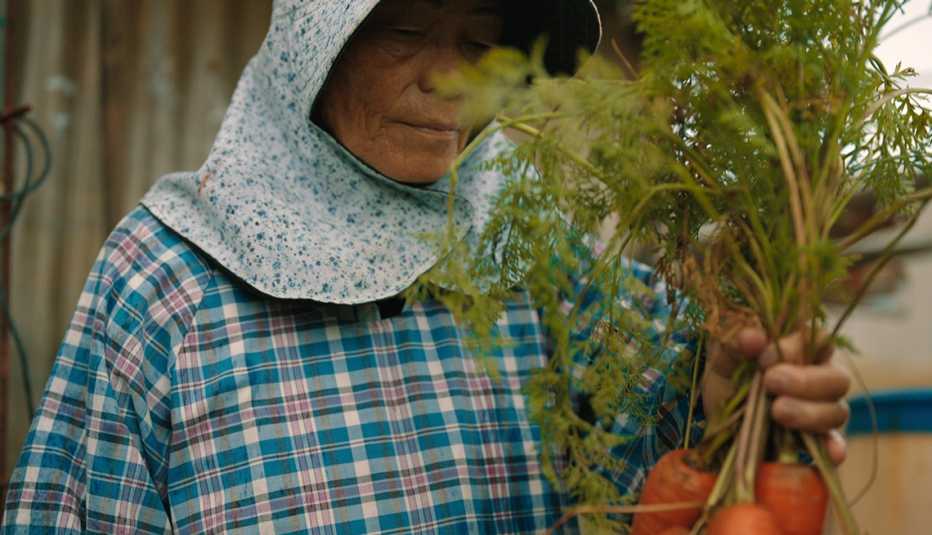 a person holding a bundle of carrots in the netflix docuseries live to 100 secrets of the blue zones