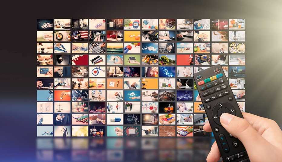 A person holding a remote control in front of a wall displaying of dozen of screens showing content