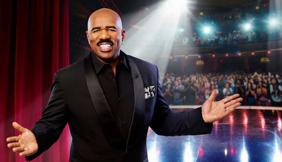 portrait of steve harvey with arms outstretched on a stage with audience behind