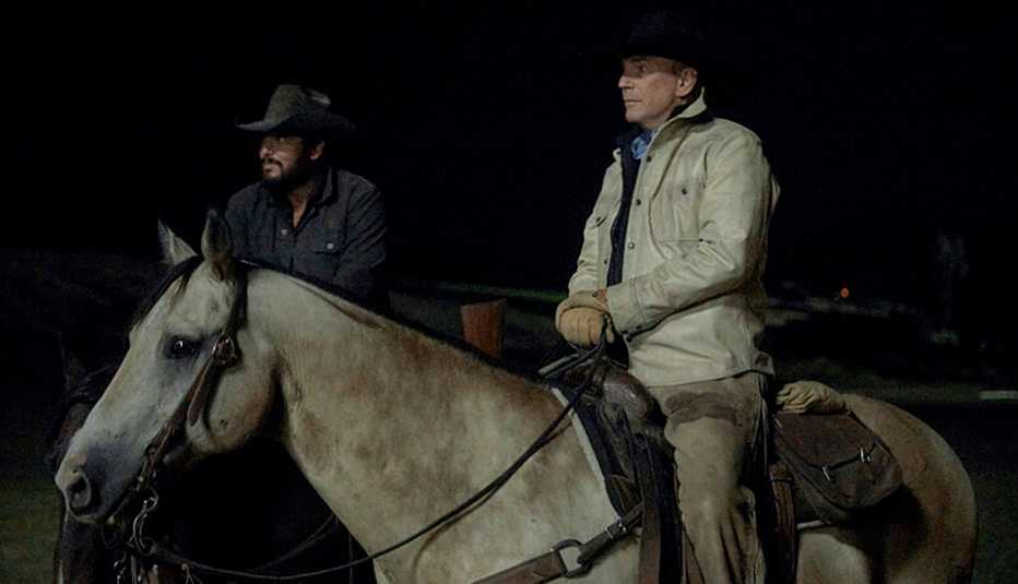 Cole Hauser and Kevin Costner riding on horses at night in Yellowstone