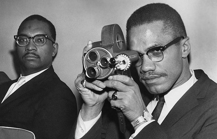 African-American Muslim minister and civil rights activist Malcolm X holding a movie camera, Historical Review of Leading Black Civil Rights Organizations African-American Muslim minister and civil rights activist Malcolm X holding a movie camera, Historical Review of Leading Black Civil Rights Organizations