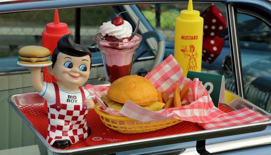 dining tray attached to a classic car window filled with a meal and a bobs big boy figurine a bobs big boy tray