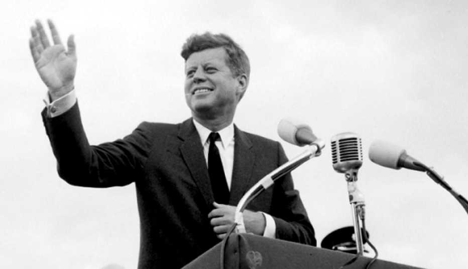 president john f kennedy waving from an outdoor podium 