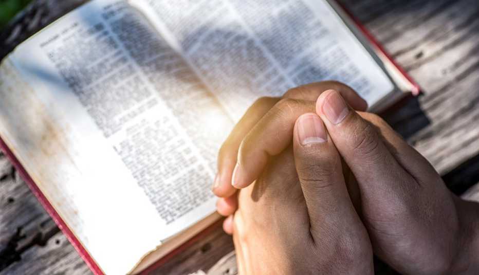 hands folded as if in prayer over a bible on a wooden surface