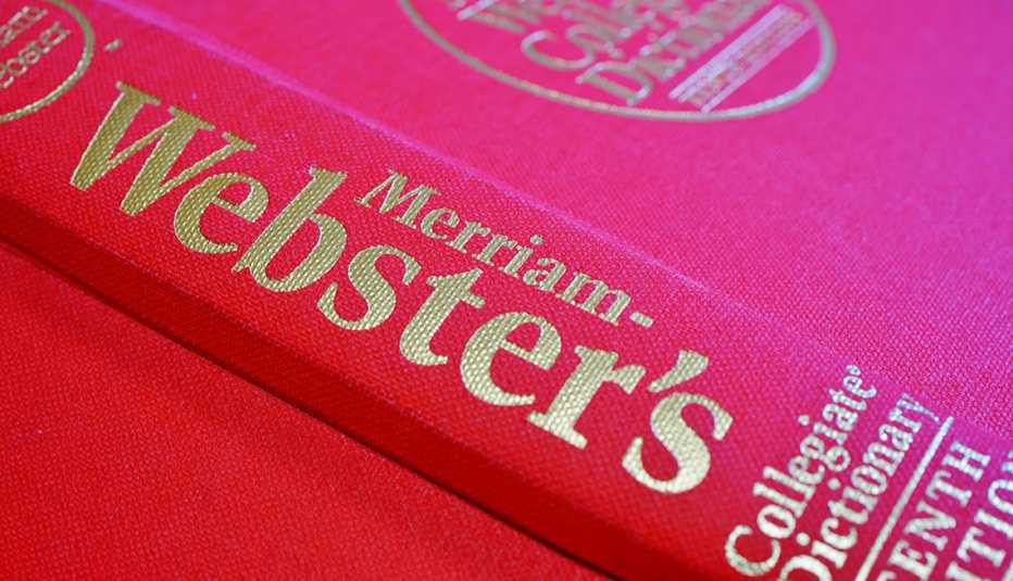 A Merriam-Webster English dictionary with a red cover sits on a desk.