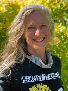 photo of a smiling woman with her vocid face mask pulled. down wearing a shirt that says berkeley teachers