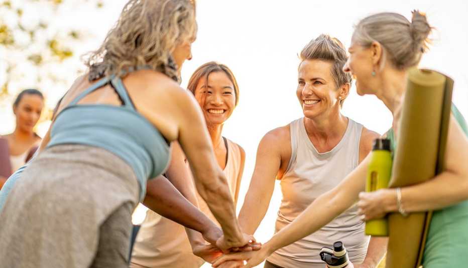 Group of mature woman smiling while holding yoga mats and water bottles at an outdoor group fitness class