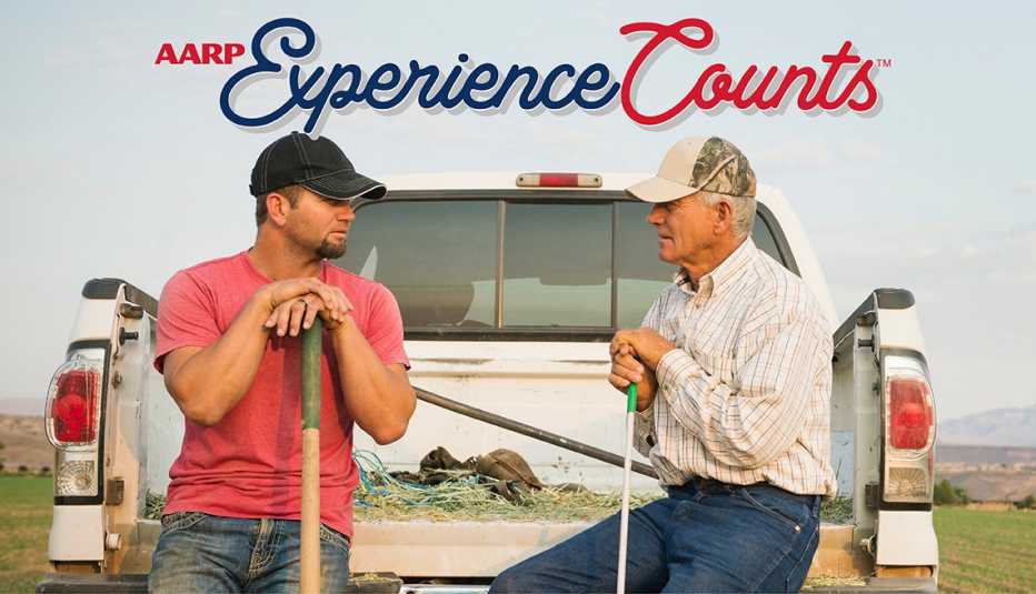 two men lean against a pickup truck while talking