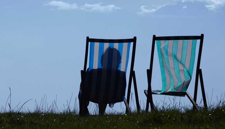 The silhouette of a woman sitting in a lawn chair next to a second empty lawn chair