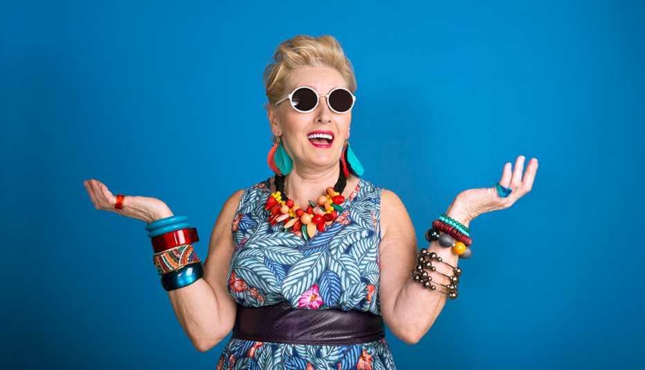 Blue background with creative, colorful mature woman standing in front of it, wearing sunglasses 