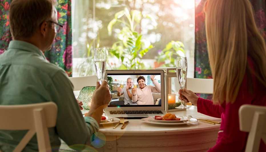 Man and woman sitting at the dining table, having dinner, drinking Champagne and having video call with senior parents on laptop. Staying home, quarantine and social distancing celebration of event.