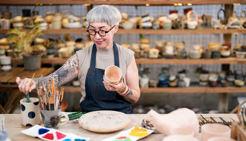 a female business owner wearing an apron works on a piece of pottery
