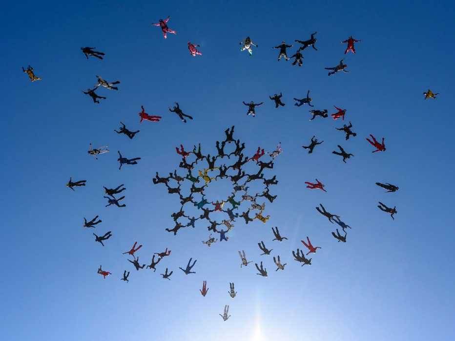 group of over fifty people skydiving and creating a linked formation as seen from below against the blue sky