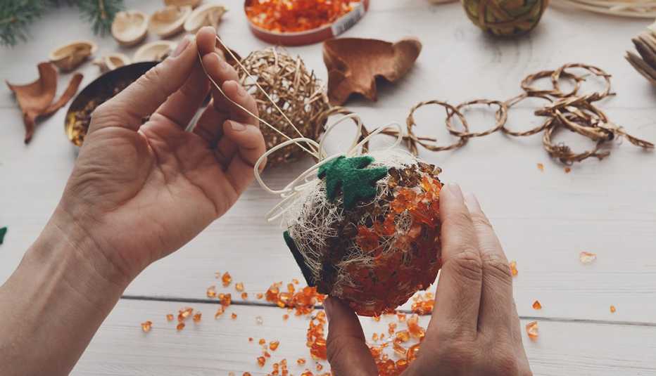 Creative diy craft hobby. Making handmade craft christmas ornaments and balls with felt spruce tree. Woman's leisure, holiday decorations. Closeup of female hands at white wood background