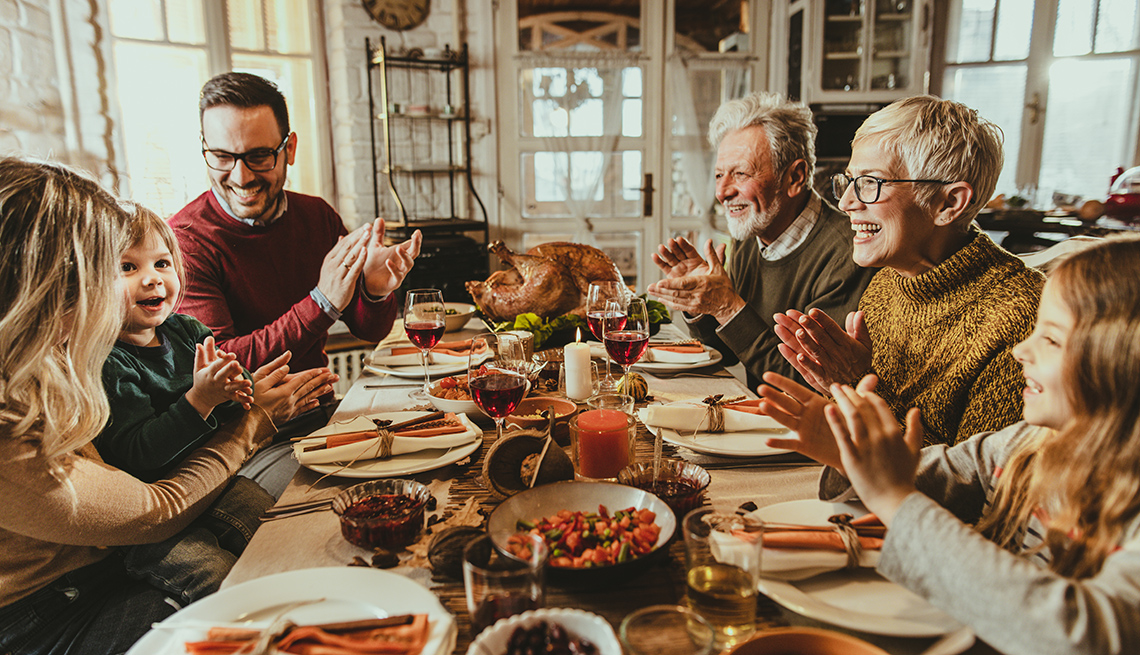 Happy multi-generation family clapping their hands while having Thanksgiving lunch in dining room.