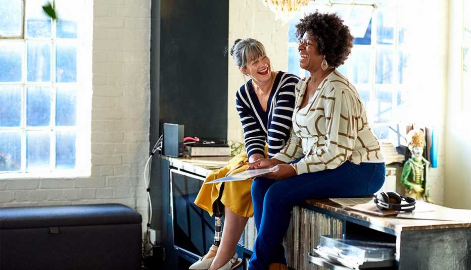 Two female friends sitting on sideboard 
