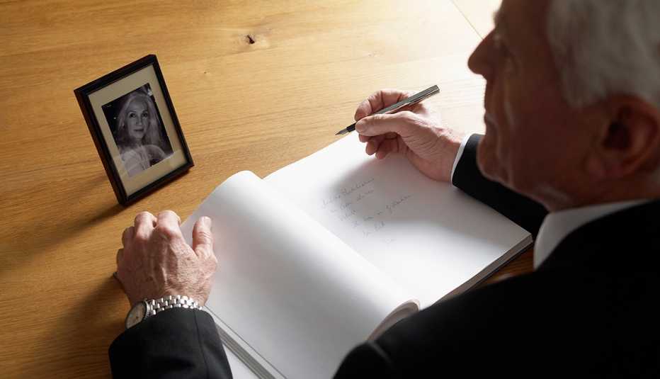 man sitting at a desk with a pen and notepad writing a eulogy while looking at a picture of his late wife