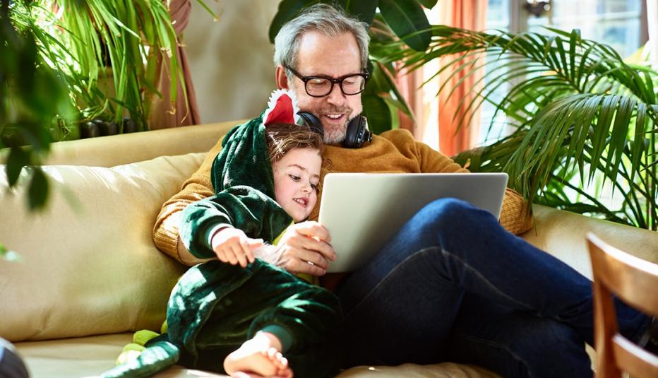 young girl cuddling with grandfather on sofa and playing online games together young girl cuddling with grandfather on sofa and playing online games together