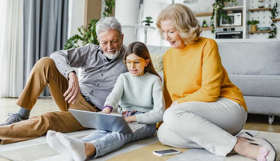 Grandparents are in the living room with their granddaughter using a laptop and smiling