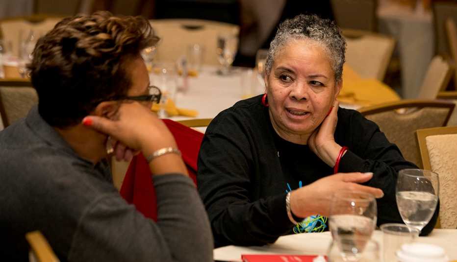 Two older women talk at a table during an event