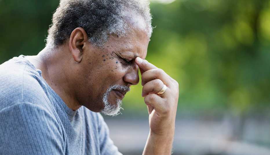 a man sitting outside, rubbing space between his eyes in pain