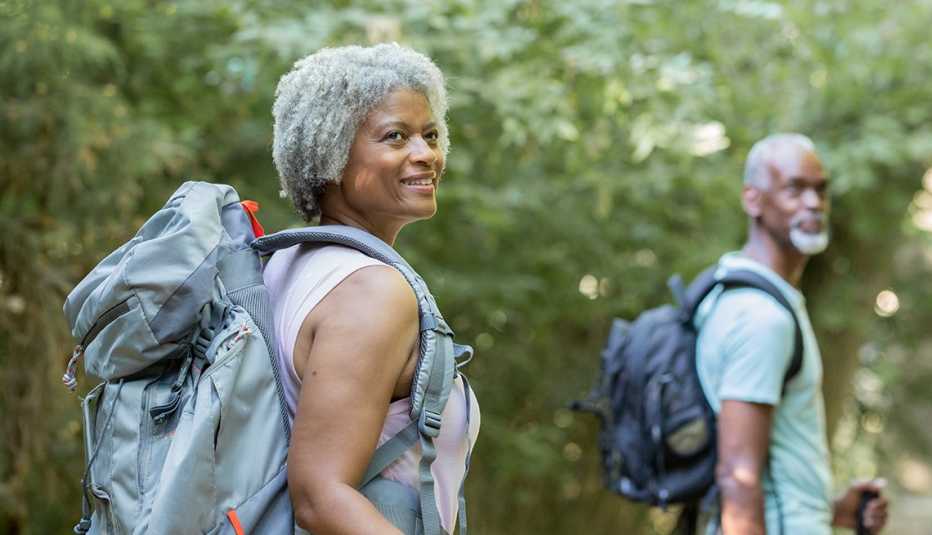 a smiling couple walks with backpacks through a beautiful forest