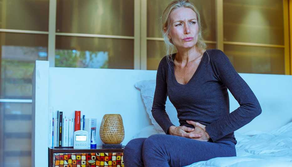 Mature woman sitting on her bed, holding lower abdomen in pain. 