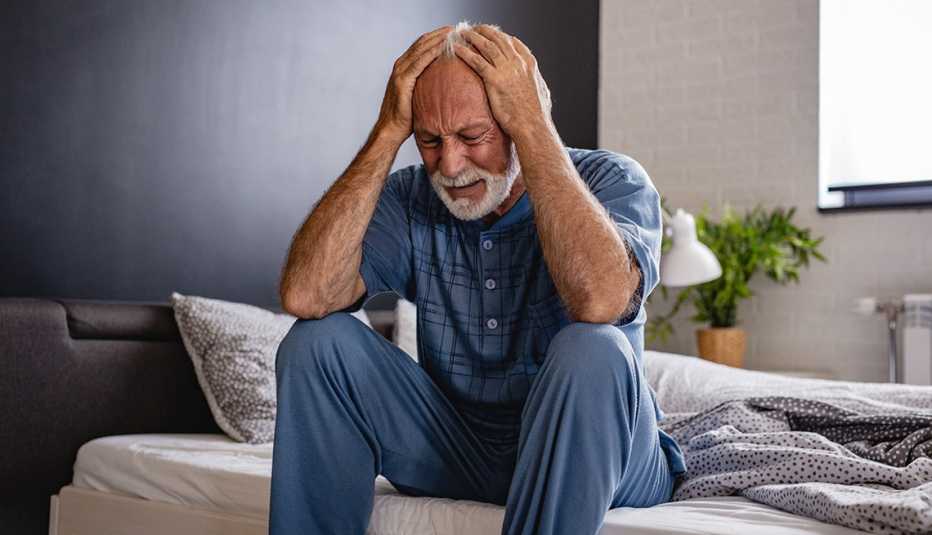 man sitting on the edge of his bed, holding his head in his hands, looks distressed