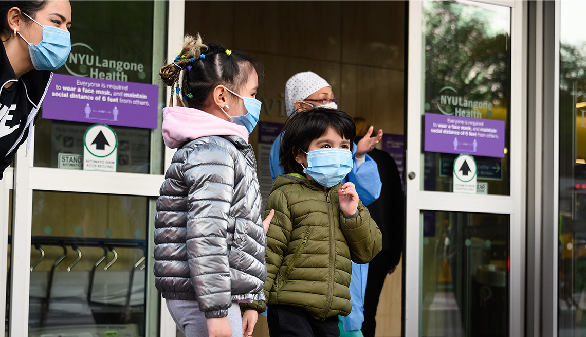 Two children stand outside hospital doors with hospital staff.