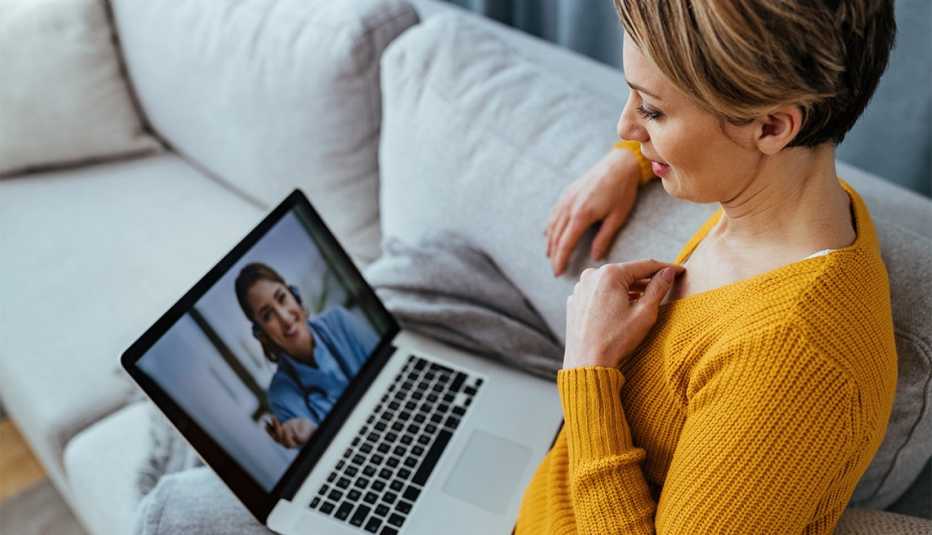 woman sitting on the sofa while talking with her doctor over a laptop.
