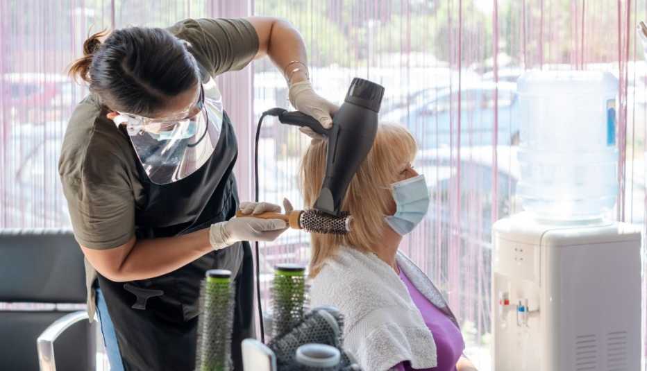 Woman getting her hair styled at a salon. Both the woman and her stylist are wearing face masks and gloves.