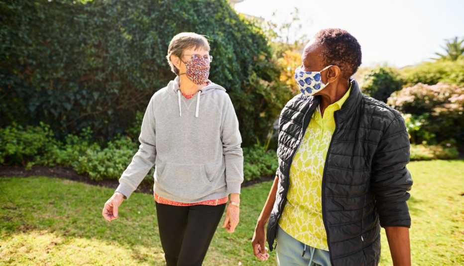 two women walking outdoors while wearing face masks