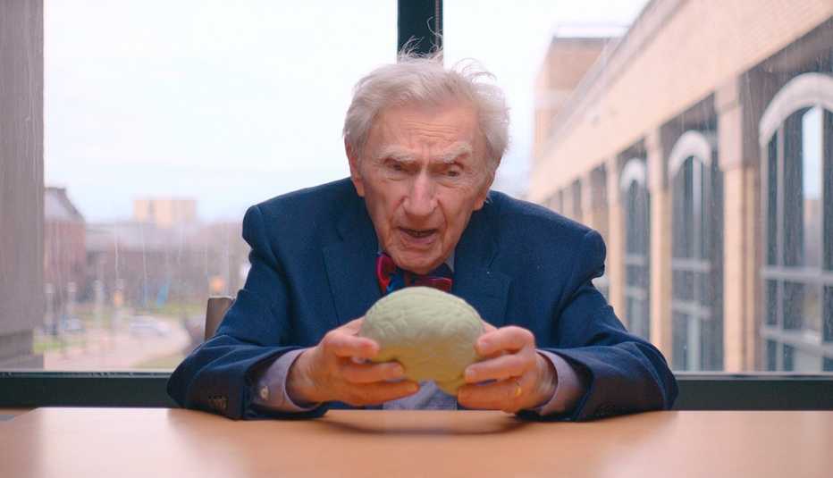 the worlds oldest doctor howard tucker looks at an object while seated at a desk in front of a large window