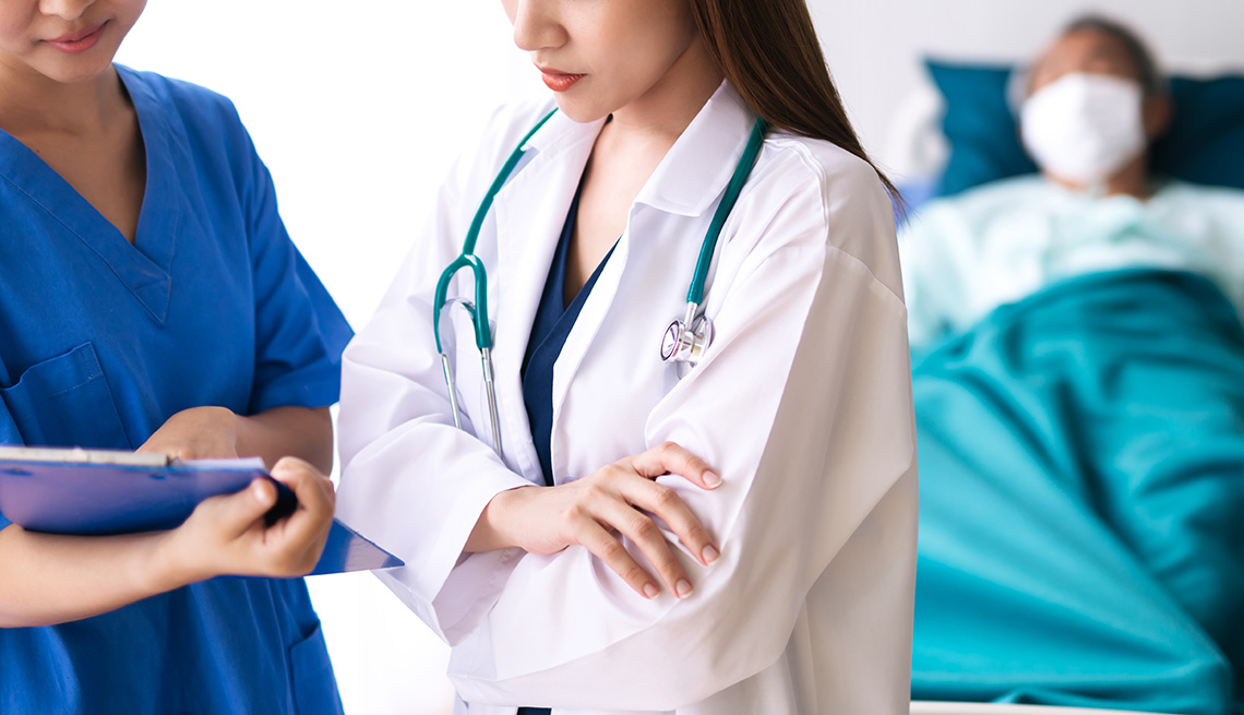 Doctor and nurse discussing a patient lying in a hospital bed. He is wearing a mask.