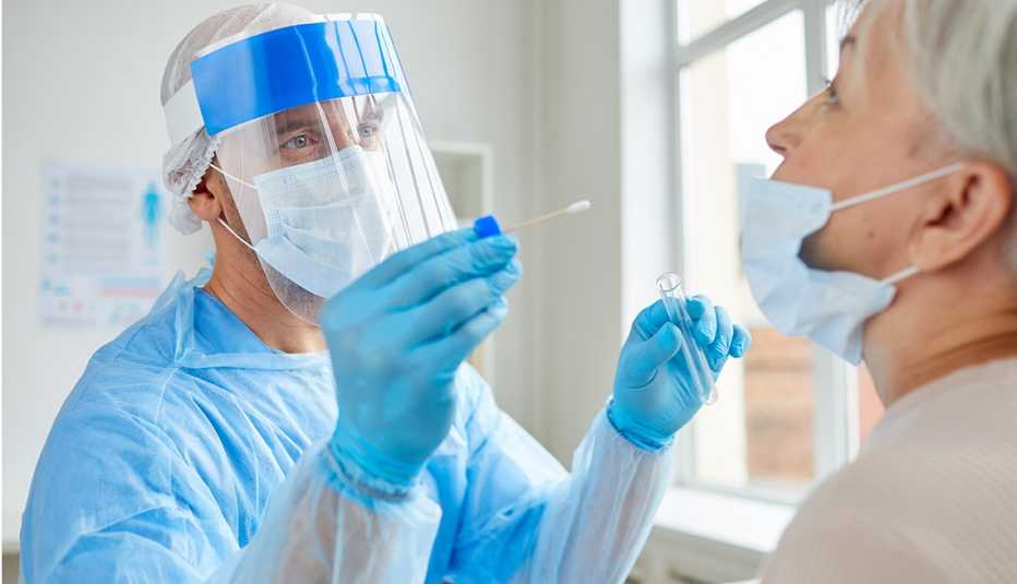 Medical worker wearing personal protective equipment testing an older woman for COVID. 