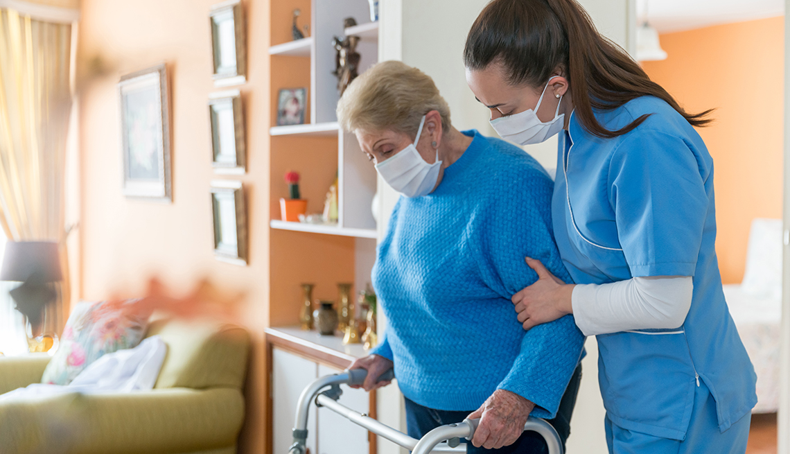 Nursing home worker helping woman with a walker. Both wearing face masks.