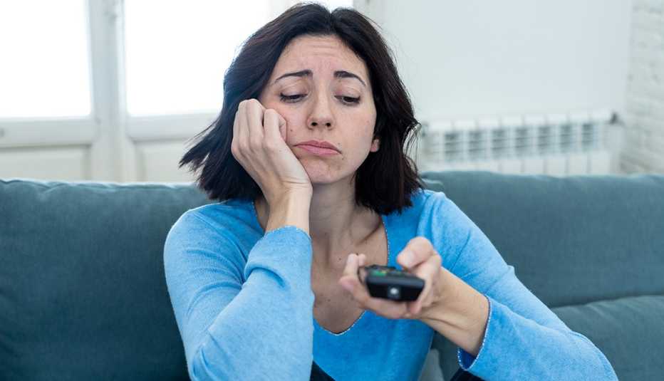 Woman sitting on the couch flipping the television with a remote looking bored
