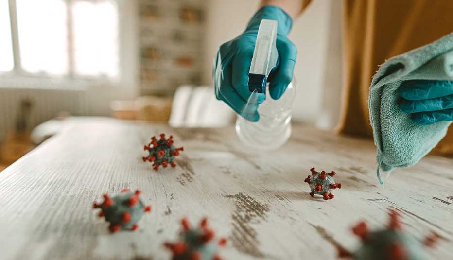 Cleaning off a table with a disinfectant, illustrations of the coronavirus are on top of the table.