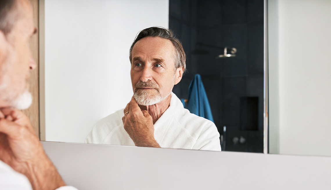 man in bathrobe inspecting his skin in mirror