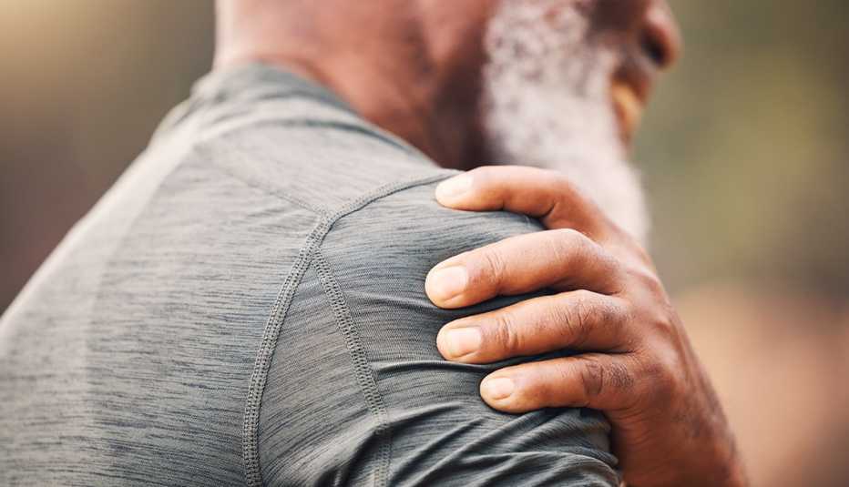 close up of a man in a gray shirt holding his upper arm in pain close up of a man in a gray shirt with a sore arm from flu shot