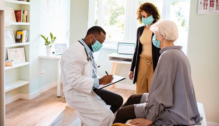 A woman and her adult daughter talking with a doctor in his office. All are wearing face masks