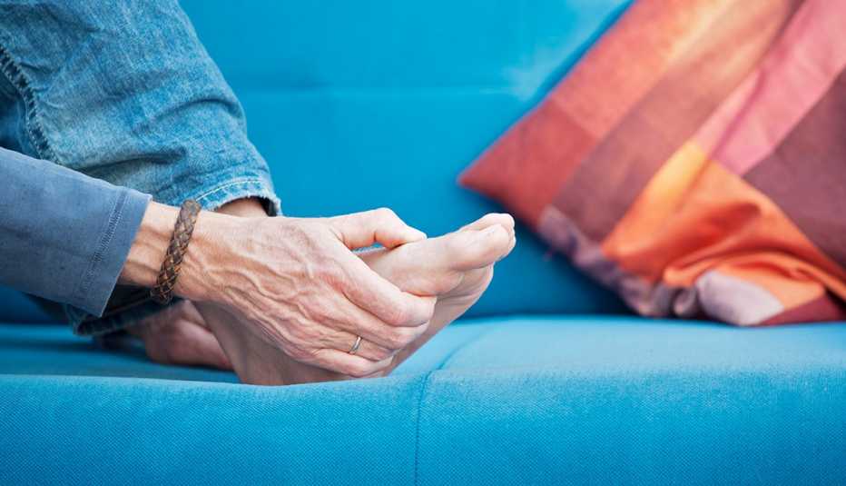 woman's hand massaging her foot, which is in pain while sitting on a blue couch