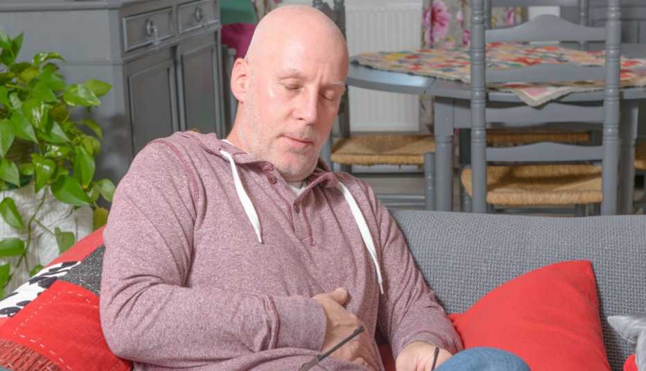 man sitting on a couch clutching his stomach 