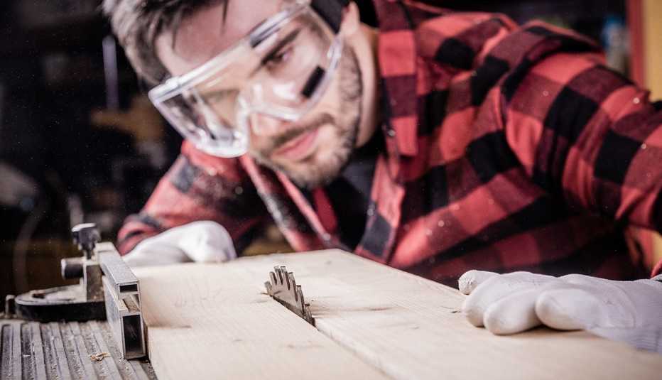 Male carpenter working with a wooden plank. He is wearing eye protection but not ear protection.